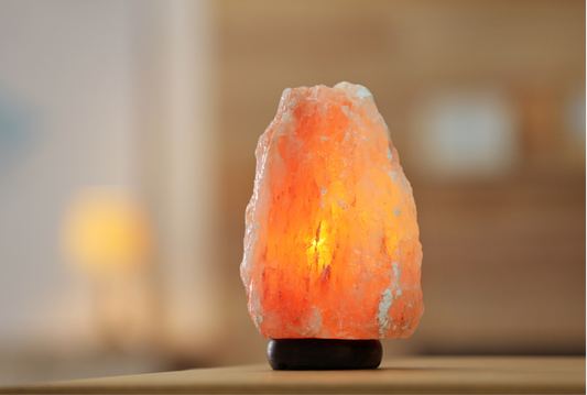 Hand-carved large amber Himalayan salt lamp on a smooth wooden base, glowing softly with warm light, displaying natural pink and orange hues.